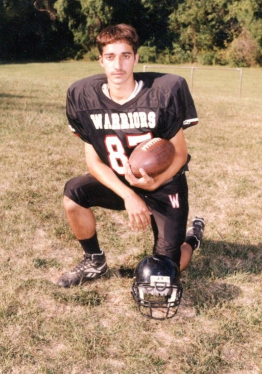Adnan in high school holding a football and wearing a football uniform