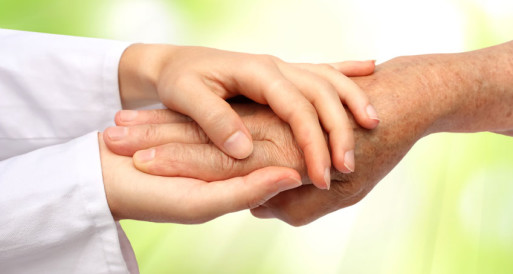 A caregiver's hands gently hold the hand of a patient