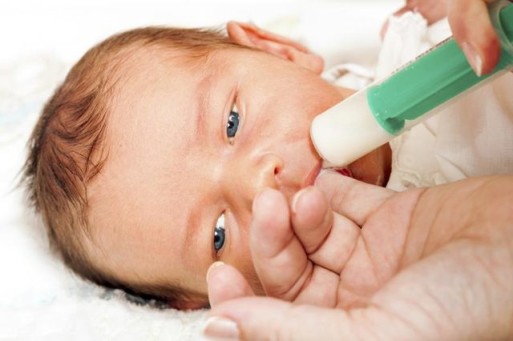 sick infant being fed breast milk with a syringe
