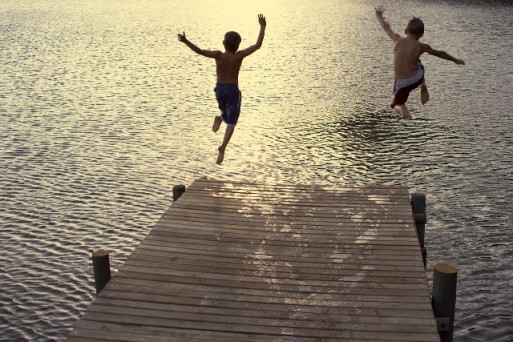 children jumping off a pier into a lake