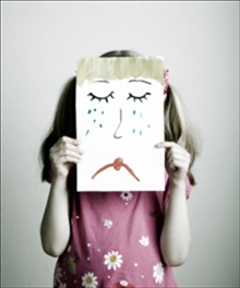 A grieving child holds up a picture of a sad face covered with tears