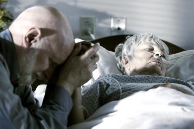 A man holds the hand of his dying wife