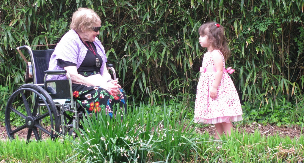 elderly woman in wheelchair faces little girl standing in pink dress