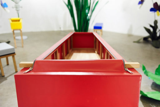A bright red, zip-up coffin that has been unzipped to reveal the square undercarriage inside