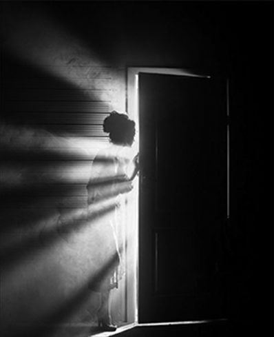 A woman looks through a sunlit door.