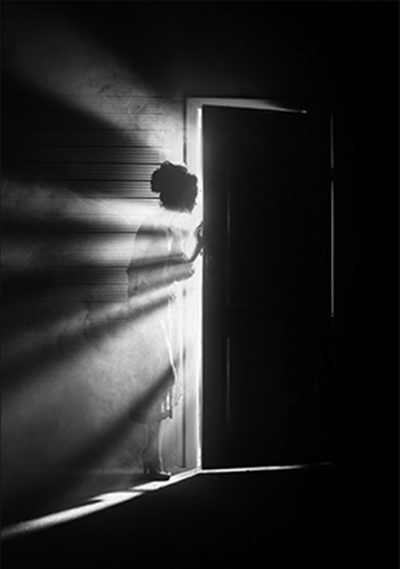 Woman standing in a dark room opening the door to the light of healing 