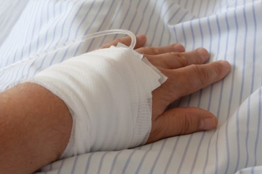 An inpatient's hand is wrapped in gauze and is resting on a hospital gown