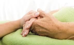 A person holding the hand of a dying loved one