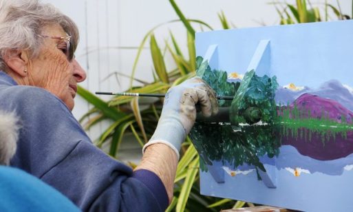 An elderly woman paints a DIY coffin 