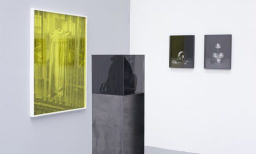 Peter Watkins' series The Unforgotting, featuring a yellow photograph mounted on the wall and a knapsack on a pillar, shrouded by a transparent black case 