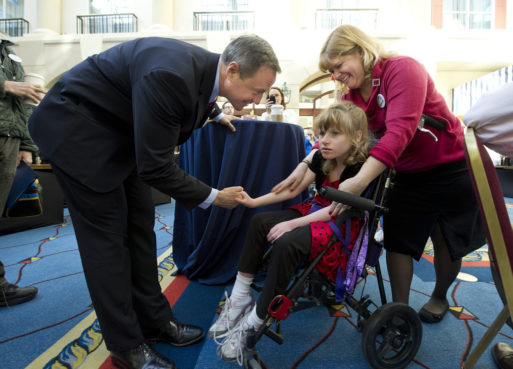 A caregiver helps a child who has cerebral palsy while she shakes hands with a politician
