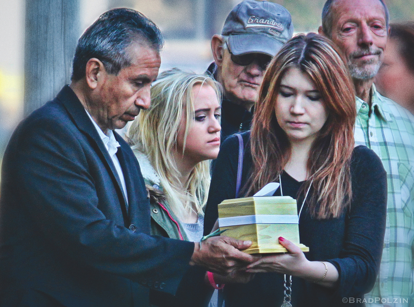 Mourners gather and pass around urns containing ashes of infants who died