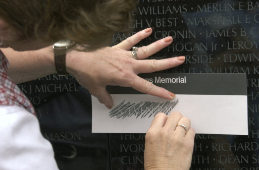 A woman copies a name on a piece of paper from a memorial statue