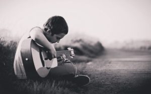 A young boy plays a guitar, to override the death rattle of someone who is dying