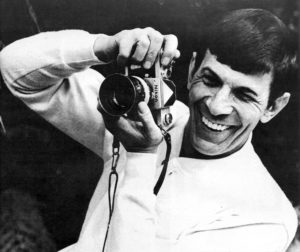 Leonard Nimoy, who played Spock, smiles while holding a camera and taking a photo