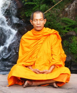 A monk sits in a yellow robe and meditates as part of his spiritual practice, which can help caregivers deal with stress