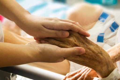 A for-profit hospice caretaker holds a patient's hand