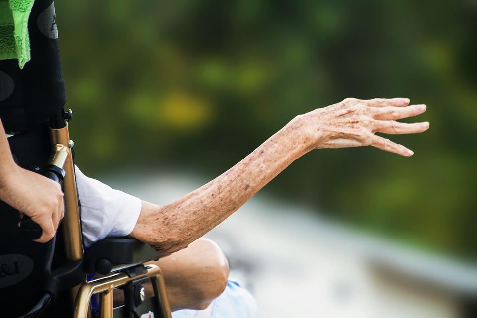 An elderly woman holds her hand out in a for-profit hospice care facility