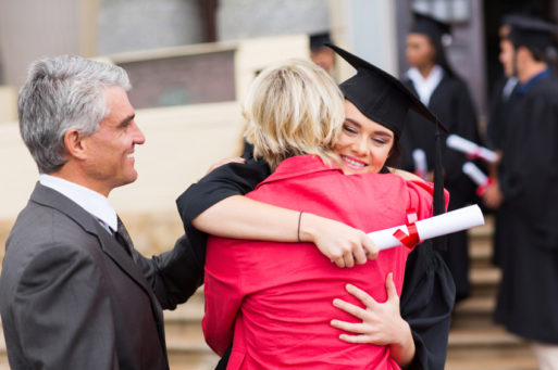 Happy young woman hugging parents at graduation despite student loan dent