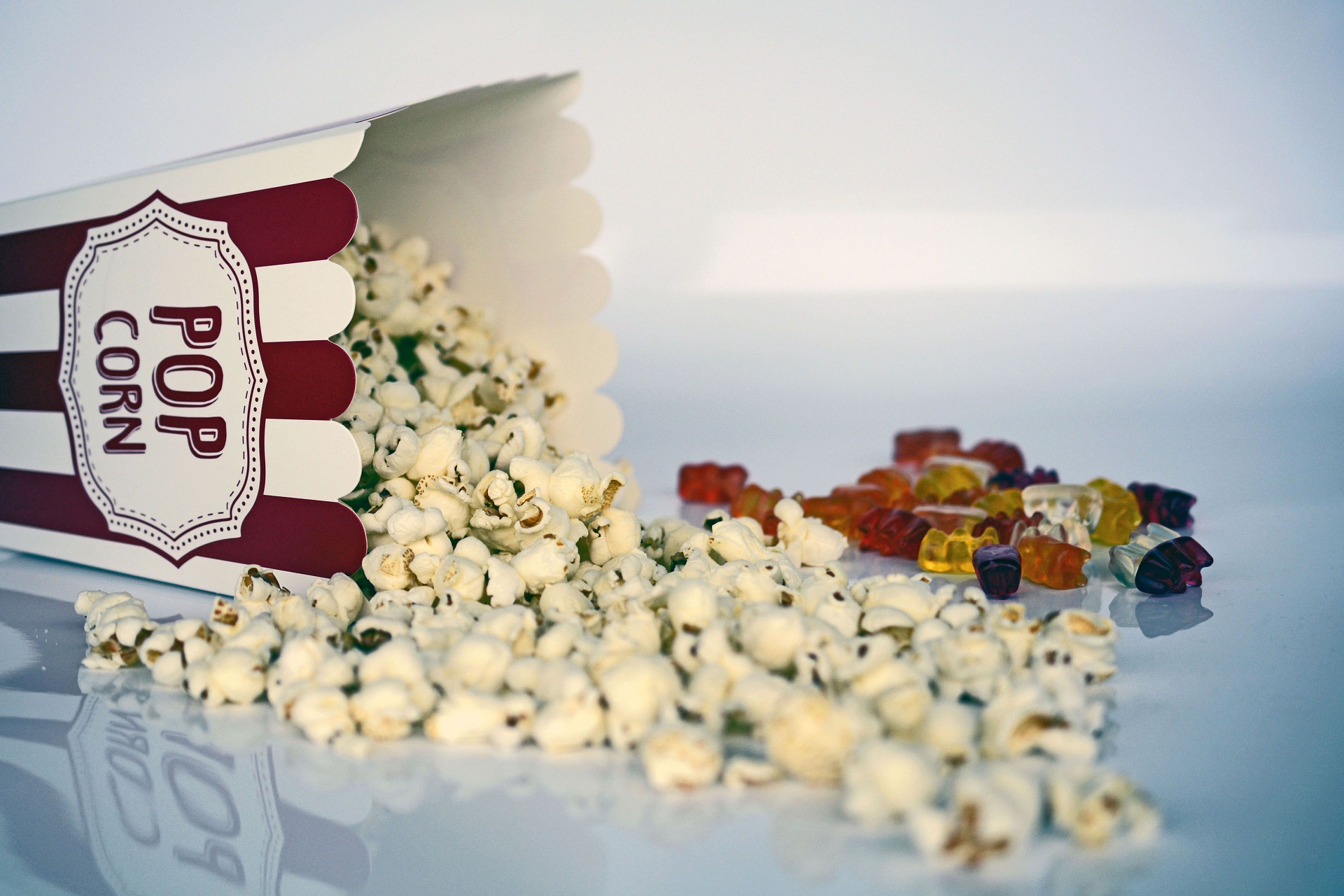Box of popcorn spilt next to candy to symbolize entertainment.