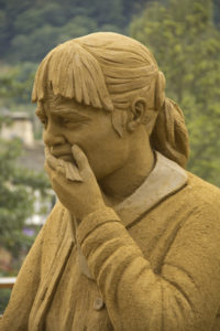 A sand sculpture of a grieving woman holding a tissue and looking like she is going to cry 