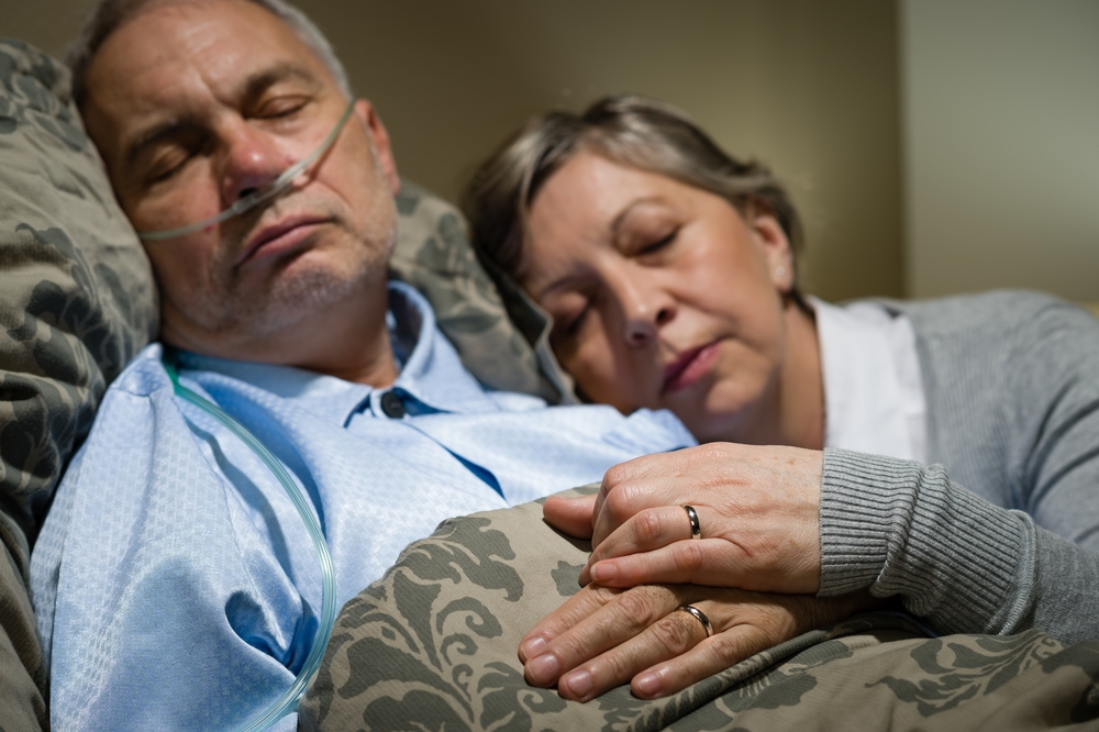 An exhausted caregiver sleeping next to her husband shows caregivers stress