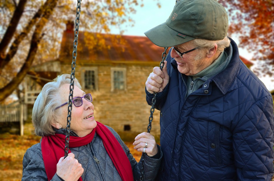 An elderly woman sitting on a swing smiling with an elderly man , friends help elder orphans thrive