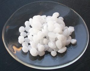A handful of white pieces of lye in a dish, commonly used in alkaline hydrolysis 