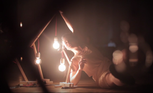 A dancer crouched next to three lightbulbs, expressing one of the five stages of grief