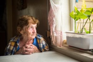 an elderly woman looking out the window experiencing loneliness
