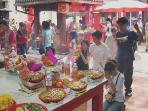 A group of people stand around a table filled with food and incense as part of a Chinese death ritual
