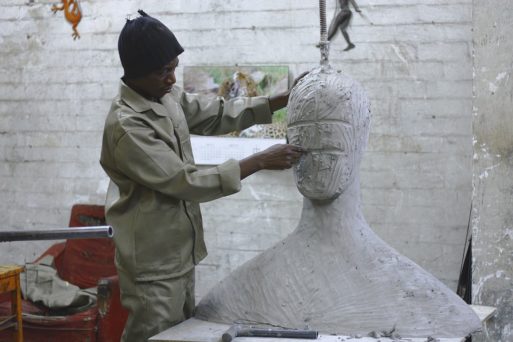 A man uses his creativity to mold a clay sculpture of a giant person on the table of an art workshop