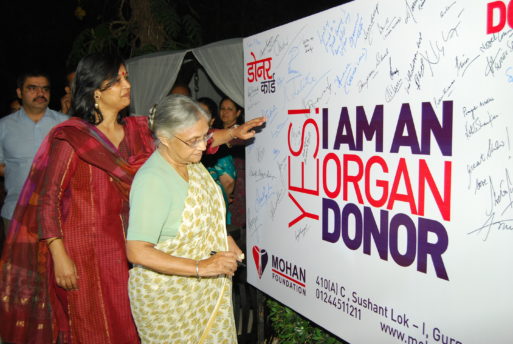 One elderly woman and one middle-aged woman stand next to a sign that says yes I am an organ donor