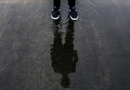 A man standing in a pool of water that shows his shadow and reflection