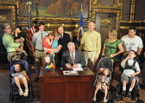 Surrounded by parents and children in wheelchairs, a governor signs a law designed to raise awareness of mitochondrial disease
