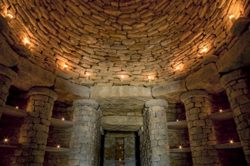 The interior of Willow Row Barrow, featuring a round, high stone ceiling with candles placed throughout the building