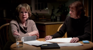 Two women investigating Sister Cathy's death on "The Keepers" sit at a table together looking at paperwork related to the case