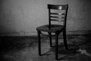 A single, lonely chair symbolizes "Empty Chairs at Empty Tables"