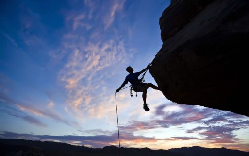 Person rock climbing against a blue sky displaying courage