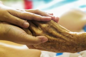 A palliative care nurse holds a patient's hand