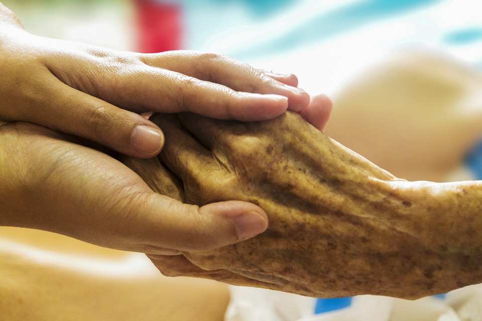 A palliative care nurse holds a patient's hand