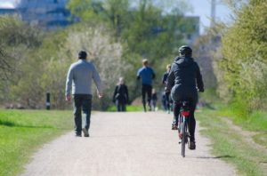 A group of people walking along a trail in a park, with one person on a bicycle riding alongside them