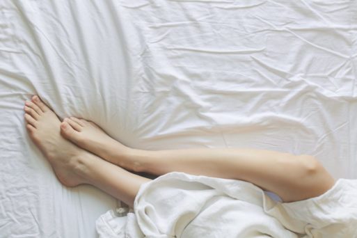A photo of a person lying in bed, with their legs sticking out from a white sheet 