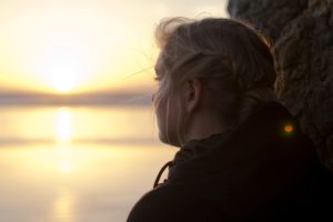 Girl looking out onto the ocean as the sun is setting symbolizing grief