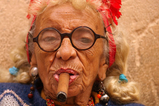 An elderly woman wearing glasses smoking a cigar