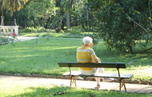 Elderly man sitting alone on park bench symbolizing aging and loneliness.