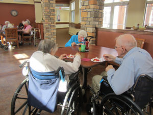 A group of elderly people sit at a table in a nursing home eating dinner