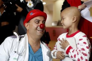 A clown doctor smiles at a young child who is staying at a hospital