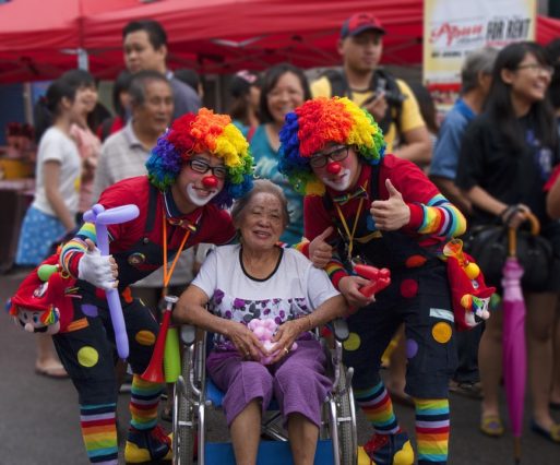 An elderly woman in a wheelchair poses with two people dressed up as clowns and clown doctors