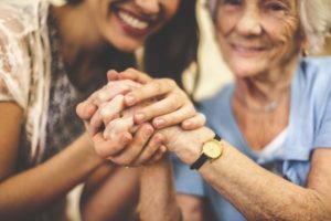 Elderly woman and young woman smiling and clenching hands together symbolizing palliative care